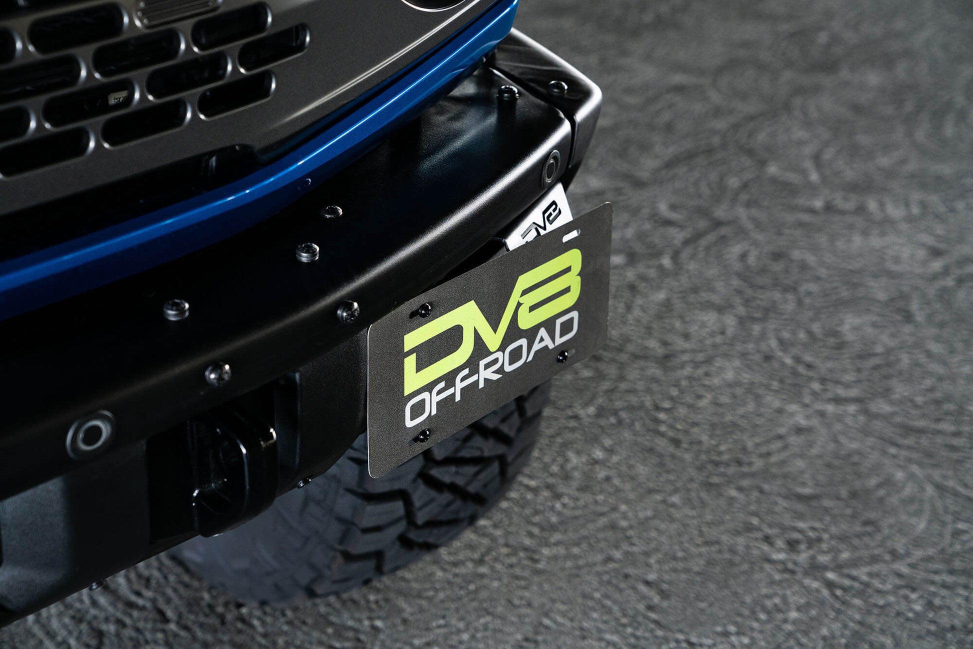 Front license plate relocation bracket places plate to the side of the bumper. by DV8 Offroad